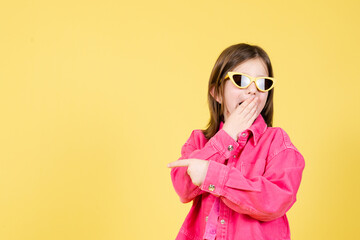 Surprised arrogant little girl pointing to the side copy space isolated on yellow background