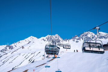St. Anton am Arlberg. March 10, 2022. Skiers sit in chairlifts on mountain slope at ski resort during beautiful sunny day, Skiers riding skilifts against snowcapped mountains