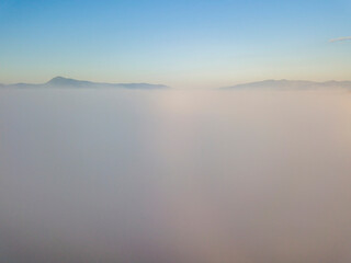 Flight over fog in Ukrainian Carpathians in summer. Mountains on the horizon. A thick layer of fog covers the mountains with a continuous carpet. Aerial drone view.