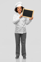 cooking, advertisement and people concept - happy smiling female chef in toque holding black chalkboard over grey background