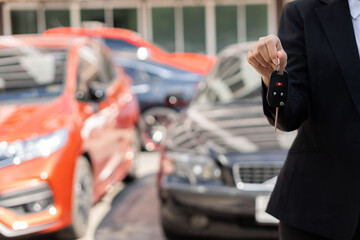 Obraz premium Businessman holding car keys in front and new car behind Parking in front of the house Offered to customers at showrooms with low-interest offers. Special promotion, transportation concept.