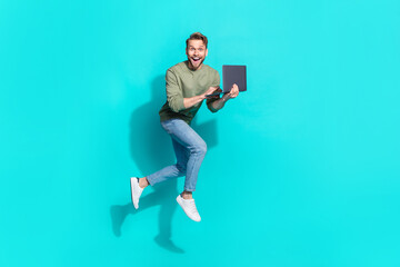 Full length photo of crazy freelancer man jump hold netbook run wear pullover isolated blue color background