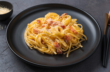 Pasta carbonara with bacon, cheese and egg on a dark background.