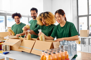 charity, donation and volunteering concept - international group of happy smiling volunteers packing food in boxes at distribution or refugee assistance center