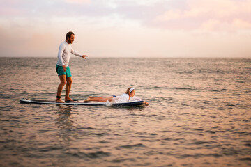 Happy father and daughter surfing on a sup board and have a funny time. Sunset ocean at the...