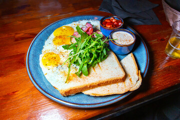 Appetizing three-egg scrambled eggs with bacon, arugula, garlic sauce and pickled beans