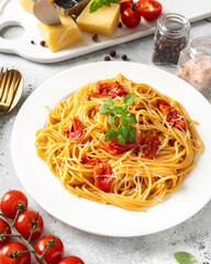 Spaghetti with tomatoes, parmesan and basil in a white plate on a bright kitchen table. Traditional Italian pasta with vegetables and cheese	