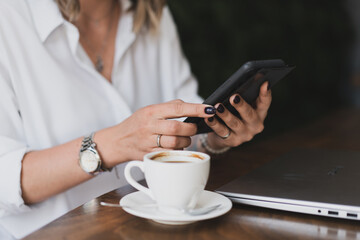 Close-up of women's hands with a phone and a cup of coffee at a table in a cafe