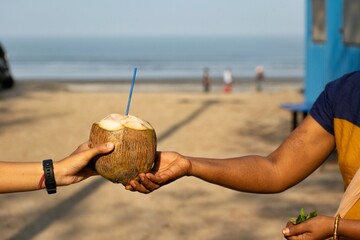 Hands of a coconut vendor selling coconut water to her customer at beach in morning. Drinking fresh...