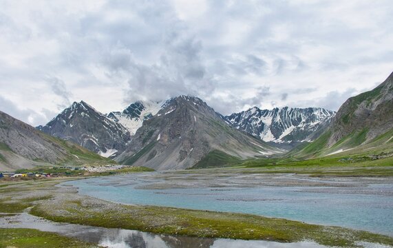 A beautiful landscape photo which includes mountains, snow, river, meadows etc 