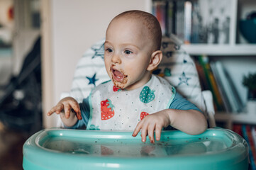 Baby boy eating chocolate while sitting in a dinning chair