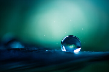 A drop of water in dark green and blue tones in the light.