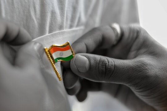 Picture of a hand of a person holding badge of Indian flag, tricolor with ashok chakra. Concept of freedom, independence, patriotism, nation, love, respect, salute, flag, republic, white, saffron.