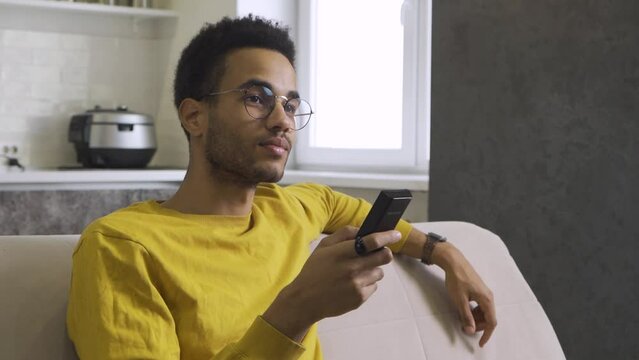 African-american young man with glasses watching tv at home.
