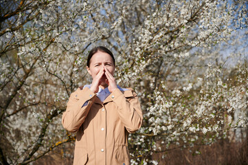 Woman allergic suffering from seasonal allergy at spring, posing in blossoming garden at...