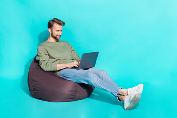 Full size photo of young blond guy type laptop wear sweater jeans shoes isolated on turquoise...