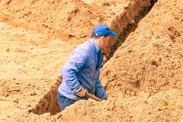 A man in blue is digging a trench. Construction works. Laying of technological communications.