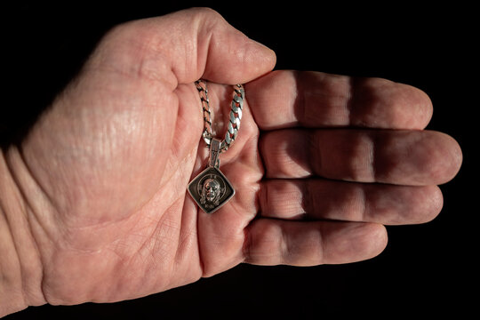 a silver chain with an image lies in a man's hand