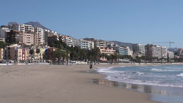Villajoyosa Spain beach with palm trees, waves and distant couple walking Costa Blanca Alicante