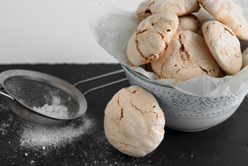 Beautiful crispy meringue with stains. Meringue on a graphite table. Powdered sugar and a sieve on the table.