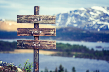 faith over fear text quote written on wooden signpost outdoors in nature with lake and mountain...