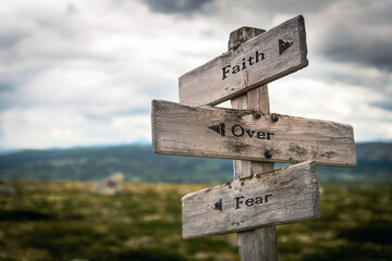 faith over fear text quote written in wooden signpost outdoors in nature. Moody theme feeling.