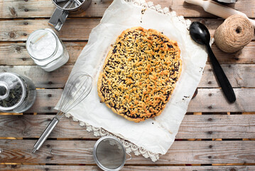 Whole grated pie on a sheet of parchment paper surrounded by kitchen utensils on a wooden table