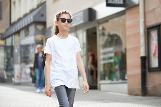 Child girl wearing white t-shirt with space for your logo or mock up outside in an urban area