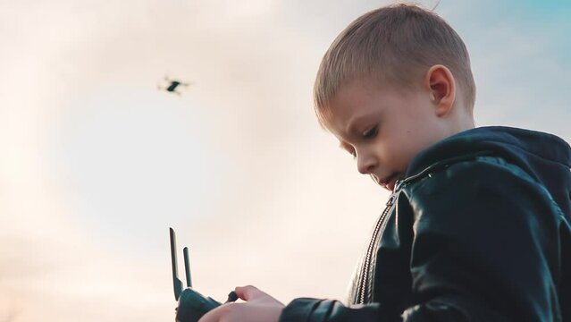 Happy boy plays with a drone in nature. Child controls the drone using a remote control.