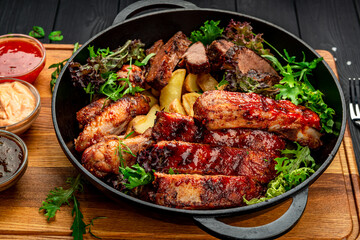 Different barbecue meat with potatoes in a frying pan