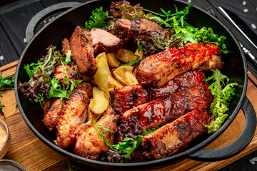 Different barbecue meat with potatoes in a frying pan