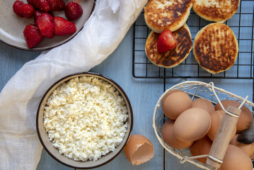 Cottage cheese, eggs, strawberries and cheesecakes on a blue countertop.