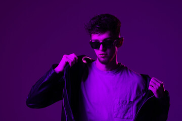 Portrait of attractive man wearing specs looking far away isolated over dark neon purple color background