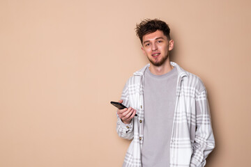 Portrait of a cheerful young arttractive man holding mobile phone wearing casual clothes standing isolated over beige background,