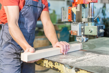 Crop carpenter cutting wooden piece on workbench