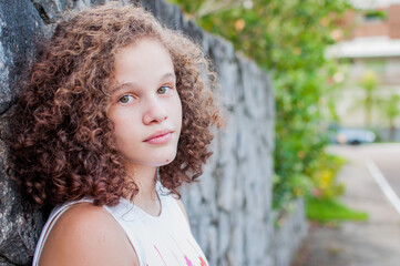 Portrait of girl leaning against stone wall - Curly hair - Copy space