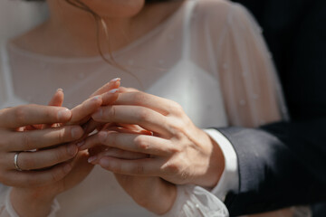  The groom hugs the bride in a white wedding dress and holds her hands close up.