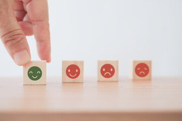 hand choose green smiling face on wooden block with blurred other behind emotion face on wooden desk for customer review, feedback, rating, ranking for service or product, mental health concept