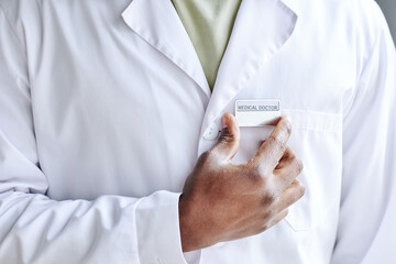 Close-up of African male doctor attaching badge on his white coat