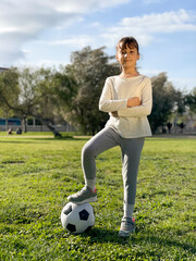 Beautiful girl has a ball at her feet with a serious look and crossed arms. Active childhood concept