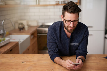 Making plans for his day of leave. Cropped shot of a handsome young man sending a text message while standing in the kitchen at home.