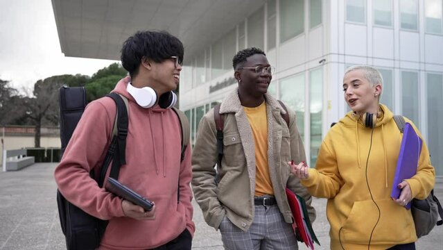 Three mixed-race young student friends walking around University Campus sharing stories laughing enjoying youth and friendship. Diversity in higher education 