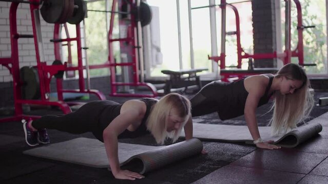 Two fit blonde women does dinamic plank exercise at gym