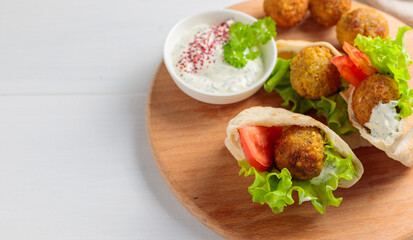 Two mini pitas with falafel, sauce and fresh vegetables. On a round wooden tray. Close-up, copy of the space