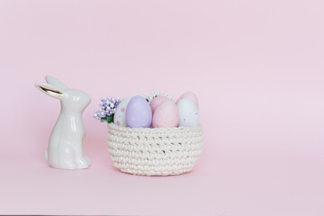 Ozdoby wielkanocne, zając, koszyk z pastelowymi jajkami, pisanki na pastelowo - różowe tło