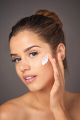 Your skin is worth investing in. Portrait of a youthful model applying moisturizer to her face in studio.