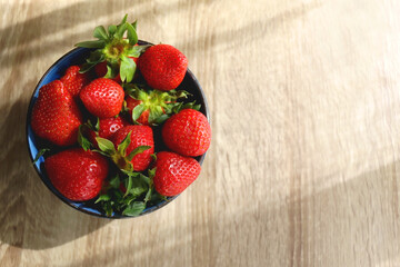 Bowl of fresh strawberries on wooden table, illuminated by sunlight. Flat lay.