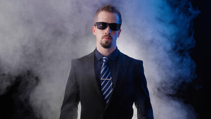 Male businessman on black background with smoke put on sunglasses posing like a boss