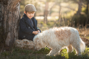 a little boy in vintage clothes walks in nature with a white shaggy dog in spring..