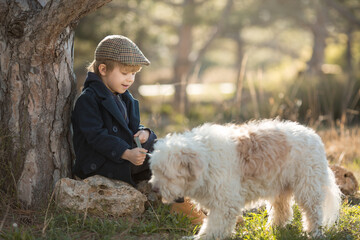 a little boy in vintage clothes walks in nature with a white shaggy dog in spring..